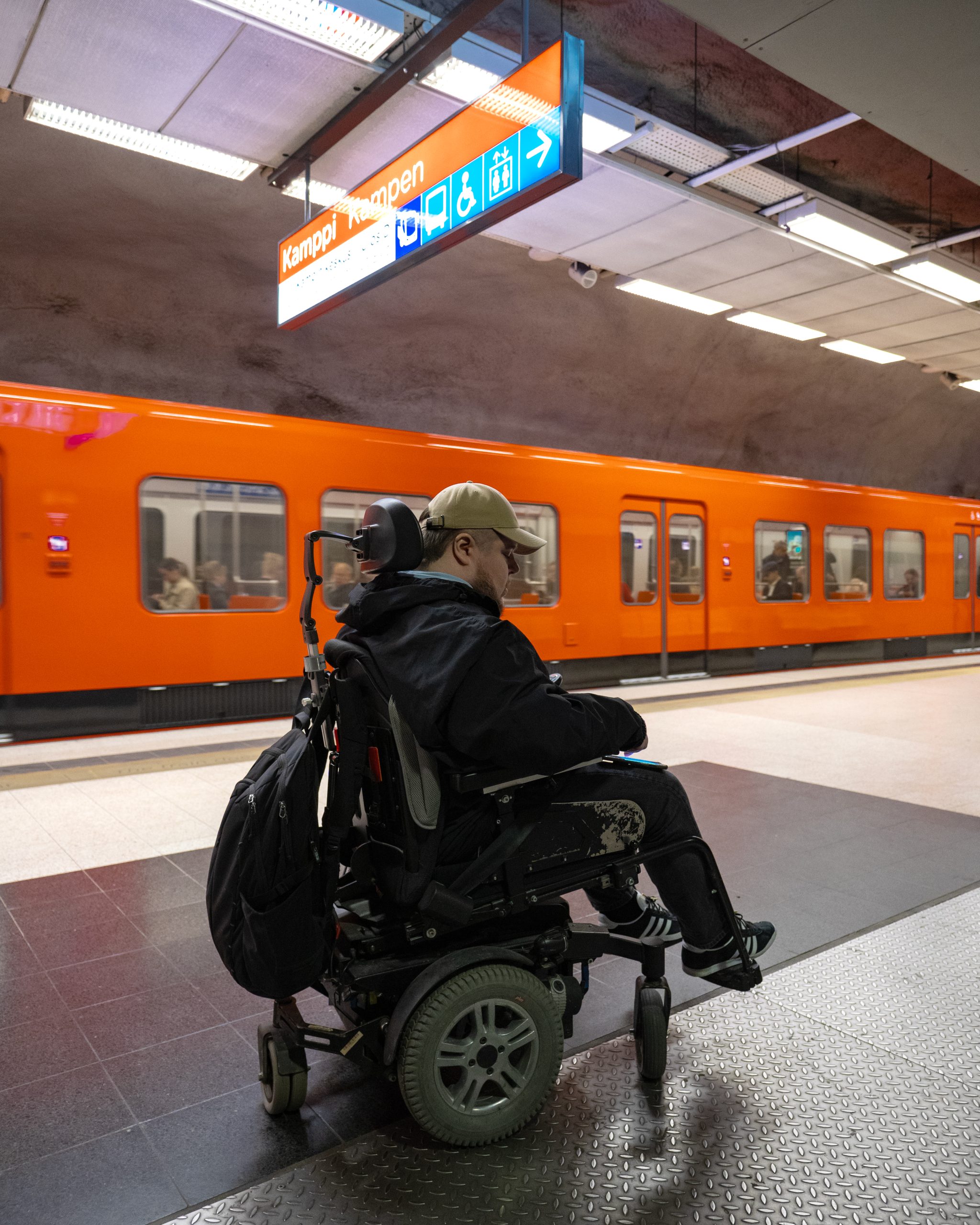 Esteettömyysasiantuntija Atso Ahonen sähköpyörätuolissaan metrolaiturilla. Takana oranssi metrovaunu.